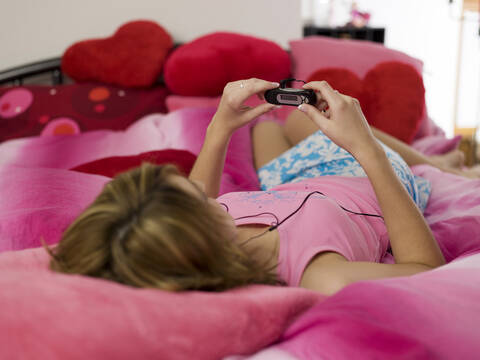 Teenager-Mädchen auf dem Bett liegend, mit mp3-Player, lizenzfreies Stockfoto