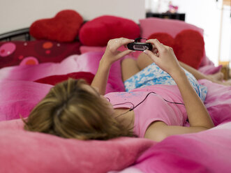 Teenage girl lying on bed, using mp3 player - KMF00429