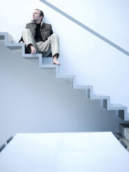 Young man sitting on stairs, low angle view - KM00493