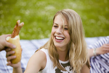 Young woman taking grilled sausage, portrait - KMF00279