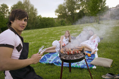 Young man grilling young women in background - KMF00267