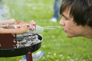 Junger Mann am Grill mit Fleisch, Seitenansicht, Nahaufnahme - KMF00266