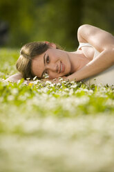Young woman lying in meadow, smiling, portrait - KMF00257