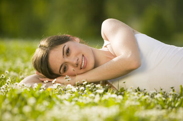 Germany, Bavaria, Munich, Young woman lying in meadow, smiling, portrait - KMF00256