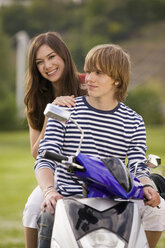 Young couple sitting on moped, smiling - KMF00235