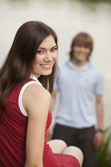 Young woman smiling with young man in background - KMF00231