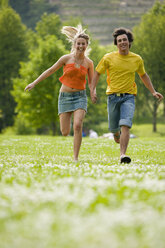Junges Paar läuft auf einer Wiese mit Hand in Hand - KMF00218