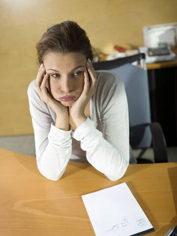 Müde Frau am Schreibtisch sitzend, Kopf in den Händen, Nahaufnahme, lizenzfreies Stockfoto