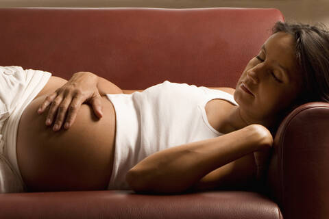 Pregnant woman lying on sofa, eyes closed, lizenzfreies Stockfoto