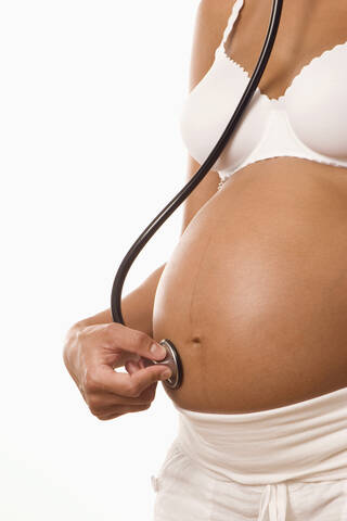 Pregnant woman holding stethoscope on body, midsection, lizenzfreies Stockfoto