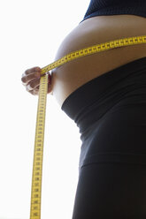 Pregnant woman, holding measuring tape, mid-section, side view - LDF00260