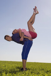 Young couple exercing gymnastic on meadow, side view - WESTF02569