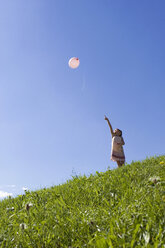Mädchen (6-7) steht auf einer Wiese und zeigt auf einen Ballon in der Luft, niedriger Blickwinkel - LDF00317
