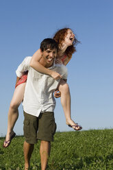 Man giving woman piggyback in meadow, laughing - LDF00244