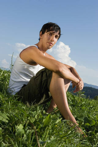 Junger Mann sitzt auf einer Wiese, lizenzfreies Stockfoto