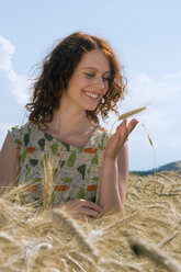 Young woman standing in cornfield, looking at cornstalk, smiling, close-up - LDF00195