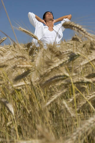 Junger Mann im Kornfeld stehend, Hand auf Hand, lizenzfreies Stockfoto