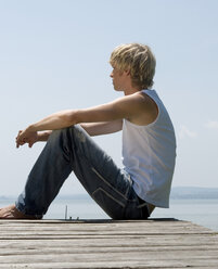 Young man sitting on jetty, side view - CLF00271