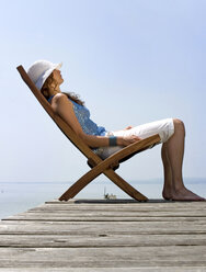 Young woman sitting on deck chair on jetty, side view - CLF00253