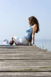 Young woman sitting on jetty, side view - CLF00243