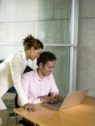 Man and woman in office, using laptop, smiling - WESTF02886