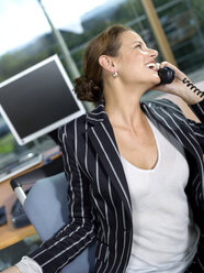 Businesswoman using telephone in office, laughing, close-up - WESTF02849