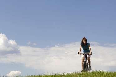 Junge Frau fährt Fahrrad auf einer Wiese - WESTF02511