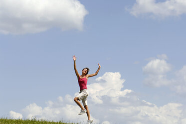 Junge Frau springt mit ausgestreckten Armen in die Wiese - WESTF02496
