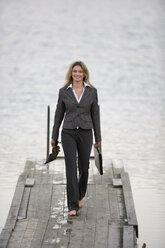 Businesswoman walking on jetty, holding shoes in hand - WESTF03067