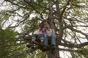 Junges Paar sitzt auf einem Baumhaus und küsst sich - BABF00223