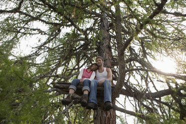 Junges Paar auf einem Baumhaus sitzend, sich umarmend - BABF00221