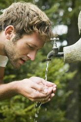 Young man cupping water from fountain, close-up, side view - BABF00218