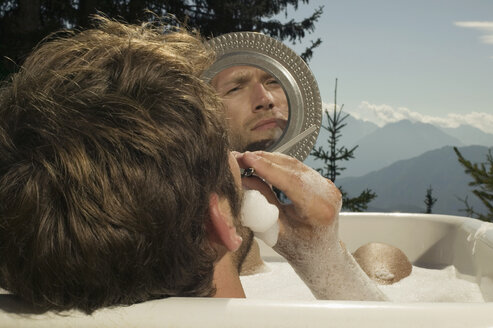 Junger Mann liegt in der Badewanne und rasiert sich - BABF00164