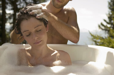 Young woman lying in bathtub, young man washing hair - BABF00154