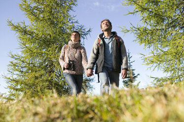 Junges Paar spaziert auf einer Wiese und hält sich an den Händen - BABF00108