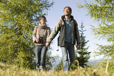 Junges Paar spaziert auf einer Wiese und hält sich an den Händen - BABF00107