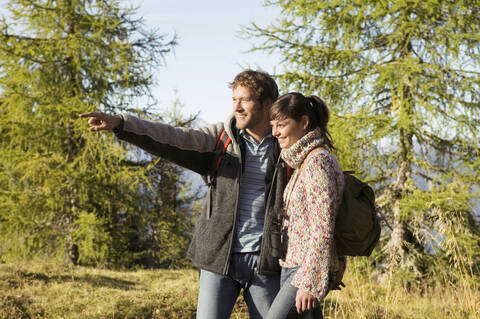 Junges Paar geht auf einer Wiese spazieren, der Mann zeigt auf die Wiese, lizenzfreies Stockfoto