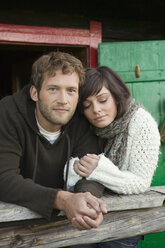 Junges Paar lehnt sich vor einer Berghütte an ein Holzgeländer - BABF00080