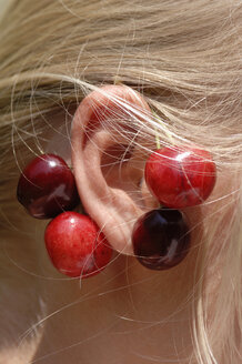 Girl wearing cherries on ear, close-up - CRF01065