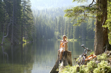 Young woman sitting on tree trunk and looking away - HHF00796