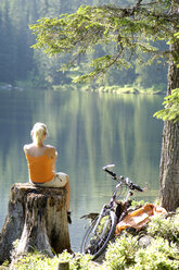 Junge Frau sitzt auf einem Baumstamm, Rückansicht - HHF00791