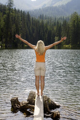 Junge Frau steht auf einer Holzplanke am See und streckt die Arme aus - HHF00788
