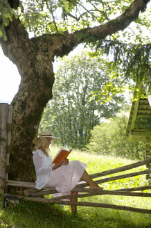 Junge Frau entspannt sich unter einem Baum und liest ein Buch - HHF00786