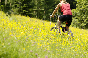 Junge Frau beim Mountainbiken im Feld - HHF00777