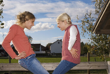 Zwei Mädchen (8-11) auf Holzgeländer, Hand auf der Hüfte, Seitenansicht - WESTF02975