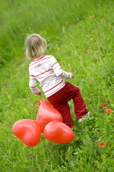 Mädchen ( 3-4 ) mit Luftballons in der Hand, auf einer Wiese spazierend, Rückansicht - SMOF00083