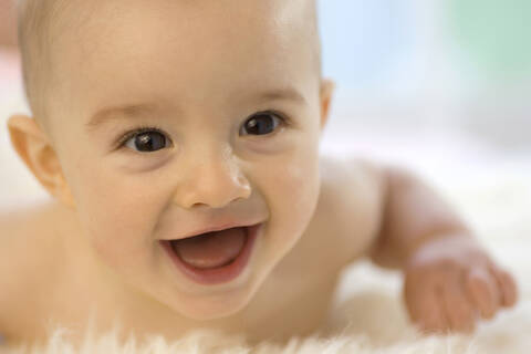 Kleiner Junge ( 6-12 Monate) auf dem Bauch liegend, lächelnd, Nahaufnahme, lizenzfreies Stockfoto