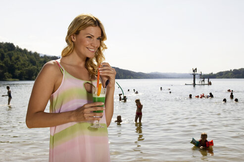 Frau hält lächelnd einen Cocktail am See - ABF00063