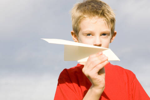 Junge (10-12) hält Papierflugzeug, lizenzfreies Stockfoto