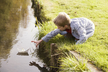 Boy (10-12) putting paper boat in river - RDF00174